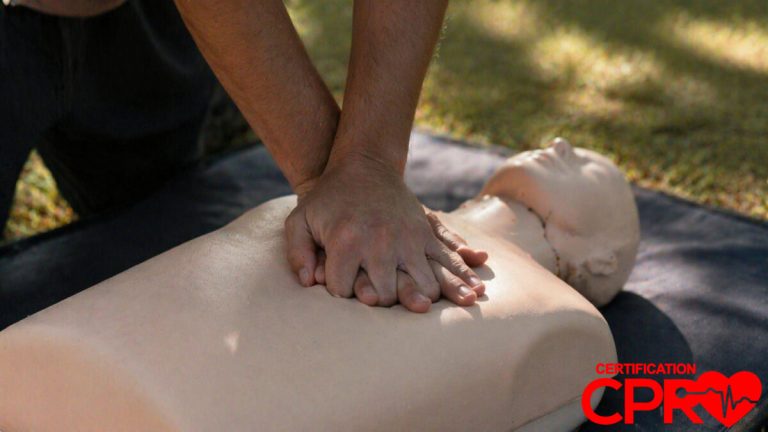Person performing hands-only CPR on a mannequin outdoors in Baltimore.